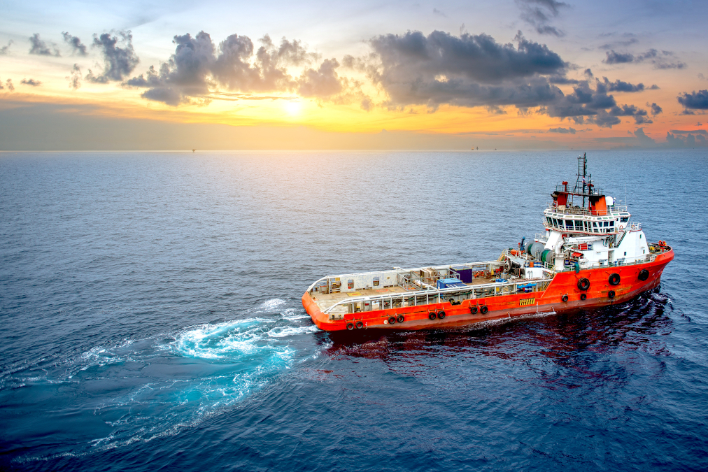 A picture of a supply boat traveling to an offshore oil rig on loading operations with cloudy sky and blue ocean background.