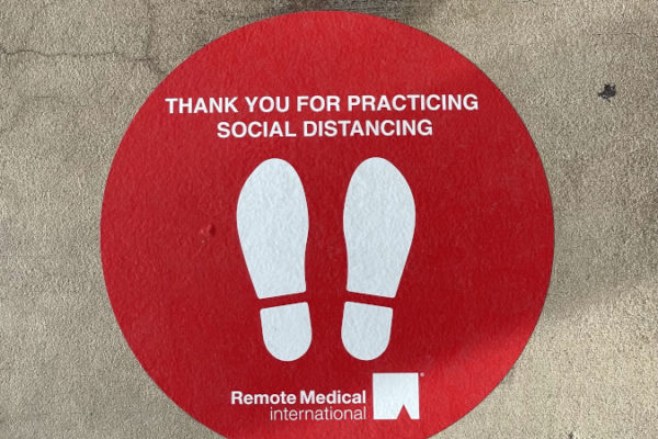 An RMI decal on the ground with a social distancing reminder.