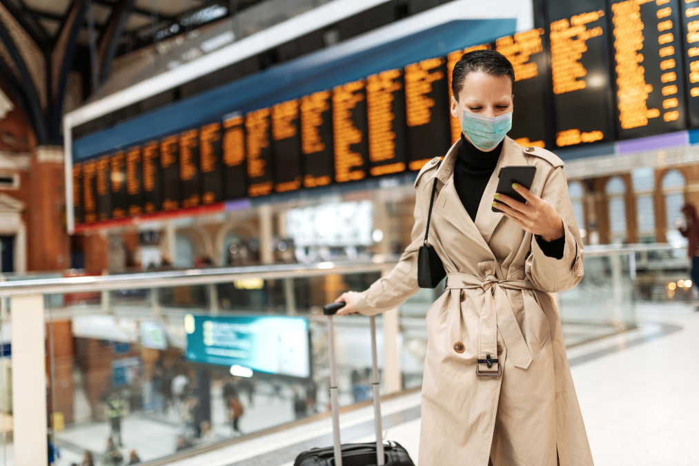 A woman wearing a face mask checking in online while waiting for her flight at the airport.